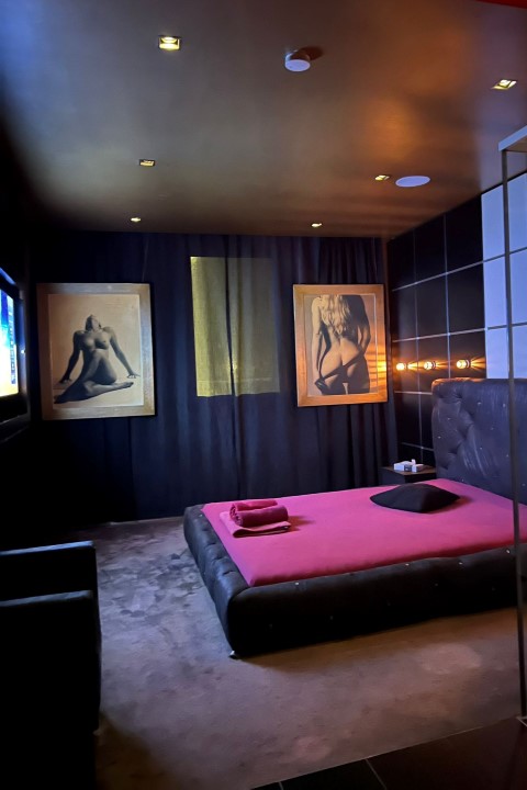 Porno Room: Bett vor dunklen Vorhängen mit zwei Aktbildern.