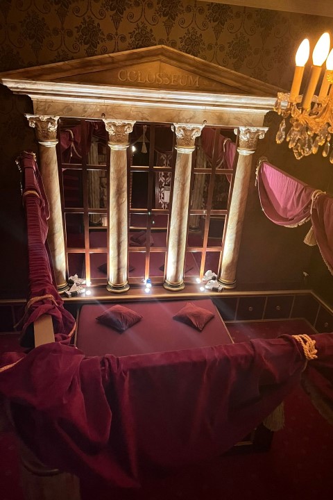 Roman Empire Suite: Tempelfront mit Säulen und der Inschrift Colosseum über dem Bett.